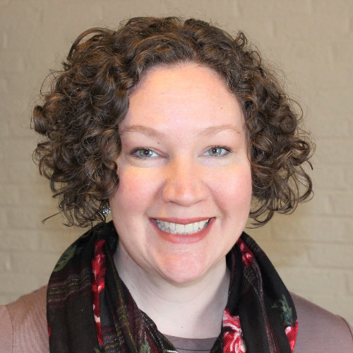 Photo of Charity Sandstrom, a white woman with brown curly hair with a floral scarf.